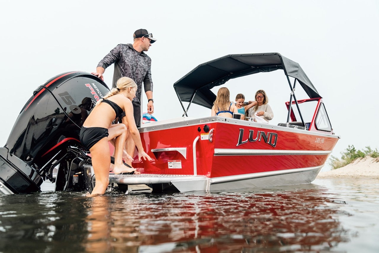 A family on their Lund Boat with a child climbing out of the water onto the boat
