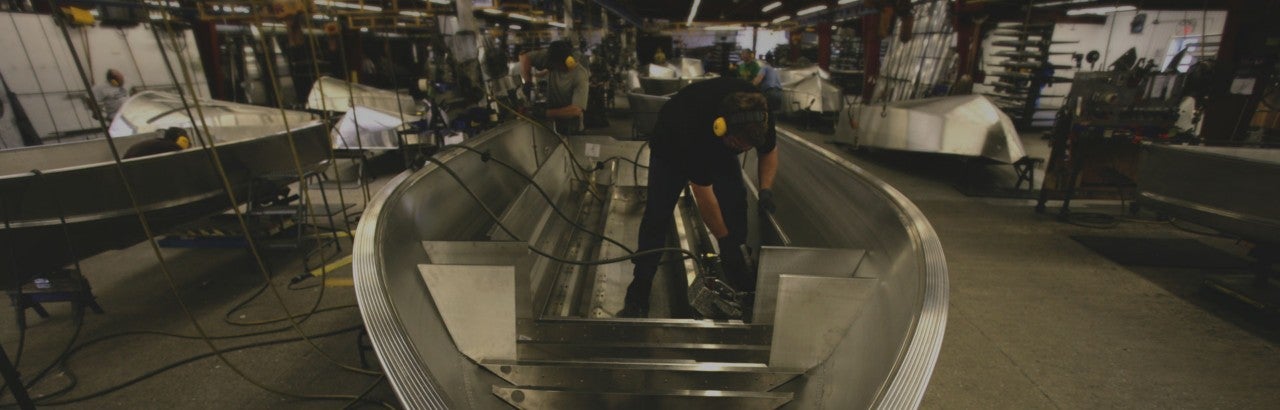 A worker welding a I beam into place on a boat hull
